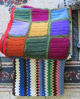 Top view of two hand crochet blankets folded on a surface, showing colorful patchwork squares with intricate crochet stitching