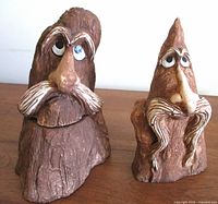 Front view of two vintage hand carved tree wizards with prominent noses, white painted beards, and hand painted eyes.
