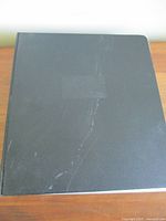 Closed view of an unmarked black binder on a wooden surface with some light wear visible.