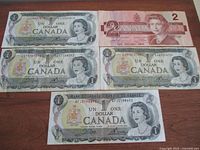 Six vintage Canadian paper money bills laid out on a wood surface, five $1 bills and one $2 bill, showing front design with Queen Elizabeth II and Bank of Canada markings.