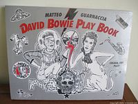 Front cover of the sealed David Bowie Play Book showing detailed artwork with Bowie motifs including figures, skull, and symbols, in black and white with red accent text.