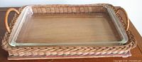 Top view showing the clear rectangular Pyrex glass casserole dish sitting inside the woven rattan basket with wood base and side handles.