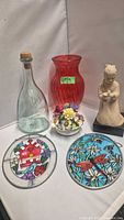 Group shot showing red vase, clear bottle, ceramic figurine, porcelain flowers, and two stained-glass panels