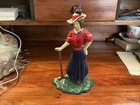 Front view of painted lady golfer cast metal doorstop on wooden surface