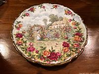 Front view of plate showing rose border, cottage scene, scalloped gilt edge