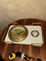 View of the brass porthole mirror, ship's clock, and white marble tray with brass handles from above, showing details of the items together.