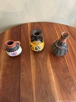 Three small vintage pottery vases on wooden table, showing front and top sides