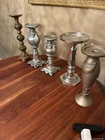 Sideview of six assorted vintage candle holders displayed on a wood table, with varying materials including wood, steel, brass, and marble.