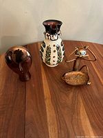 Assorted sculptures on wood table: polished copper cat statue, ceramic owl vase, Hungarian Miska kancsó wine jug
