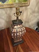 Full view of the lamp on a wooden table showing the ceramic patterned base and electric socket with bulb holder and switch.