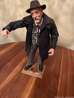 Full view of the figurine showing the man standing on the wooden base with his black shoes and gray trousers visible.