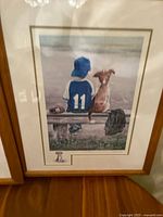 Framed signed limited edition print showing a boy in blue cap and jersey with number 11 on bench with his dog, near a lake or body of water.
