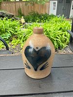 Front view of the brown earthenware vase showing the blue heart and hand-like design on the front.