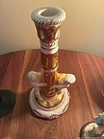 Porcelain gold and white candle holder with two cherubs, standing on a wooden surface against a plain wall.