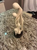 Side view of abstract white family statue figurine on black base displayed on granite countertop.