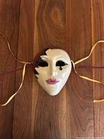 Front view of the hand-painted Venetian style wall mask showing facial features, black and green painted accents, and hanging ribbons.