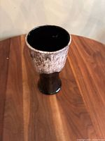 Handmade medium-sized ceramic vase with dark brown base and textured light grey top section, glossy black interior, standing on wooden surface