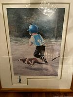 Framed, signed limited edition print by Jim Daly showing a boy in a baseball helmet running with his dog on a field