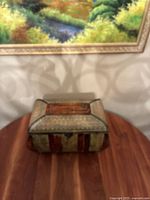 Front view of the wooden keepsake box placed on a wood table under a framed painting, showing the multicolor pattern and latch.