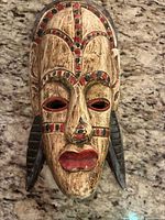Front view showing full carved wooden mask with painted red and black geometric details and large side adornments.