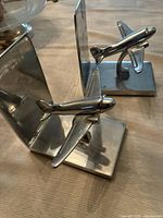 Pair of silver aluminum airplane bookends placed on a table showing both the L-shaped base and airplane figurines attached.