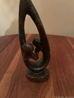 Dark greenish-black polished stone abstract sculpture showing two stylized figures within a teardrop shape on circular base, symbolizing family or unity.