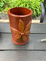 Front view of terracotta clay vase showing floral design, shape, and color on outdoor surface.