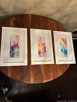 Three signed watercolor paintings on wood table, white frames with white mats