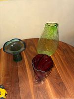 Three vintage glass vases displayed on a wooden table showing different shapes and colors