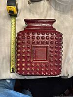 Top view of rectangular burgundy ceramic vase with raised circular studs, measuring tape shows width about 10 cm
