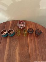 Seven vintage candle holders on wooden surface including blue hand-painted glass holders, mosaic crystal holder, yellow glass holders, and brown glass holders.