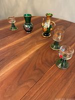 Photo showing five vintage glassware pieces on wooden table with green, gold, and clear details.