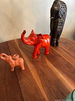 All three elephant sculptures arranged on a wood surface: small terracotta pottery, medium red ceramic, and tall carved dark wood with patterns