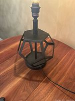 Full view of the black metal vintage table lamp on wooden surface showing geometric cage design and electric cord.