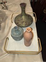 Set of three pottery pieces on white tray with gold handles: green wide vase, blue shorter vase, and terracotta bottle