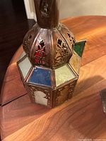 Close-up photo showing the octagonal lantern base with multicolored stained glass panels and intricate metal cut-out designs.