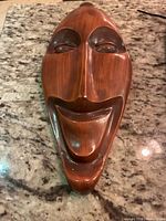 Front view of the vintage plaster wall mask showing the full face with smooth wood-tone finish and smiling expression.
