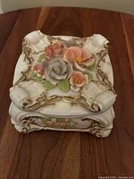 Front angle showing ivory porcelain box with ornate edges and multicolored floral decoration on the lid.