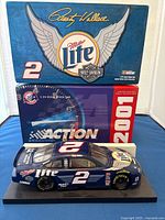 Front-side perspective of the Rusty Wallace die-cast model car on display stand, with blue and red 2001 Action box behind showing branding and signature.