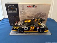 Front and side angle of the black and yellow 1991 Miller Genuine Draft diecast model car with number 2 and sponsor details, in front of original box.