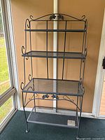 Front view of the full black wrought iron baker's rack showing all shelves and floral accents.