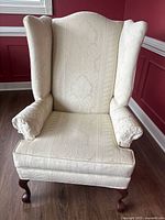 Front view of the cream wingback chair showing damask upholstery and wooden legs