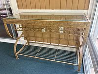 Front and side view of rectangular metal and glass wine rack table with decorative scrollwork, beveled glass top, and metal bottle rack below the tabletop.