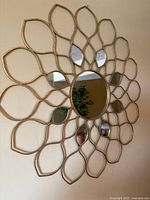 Front view of a round wall mirror with a gold metal frame forming a petal design, attached on a wall.