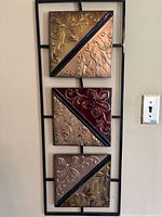 Front view of metal wall art showing three embossed floral and geometric square metal panels mounted on black metal frame.