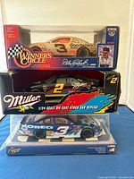 Front and side view of three NASCAR 1/24 scale die-cast model cars in original packaging.