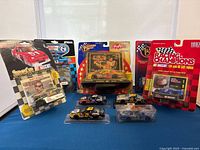 Photo showing multiple NASCAR diecast cars in original packaging and loose, along with collector's cards and display stands.