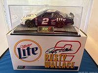 Diecast model of Rusty Wallace NASCAR car displayed inside clear protective case, resting on original branded box with Miller Lite logos and Rusty Wallace branding.