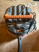 Top view of Ridgid wet/dry vacuum with orange handle, visible control switch, brand name, and attached hose.