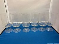 Six clear glass water goblets arranged in a row, showing overall shape and size.